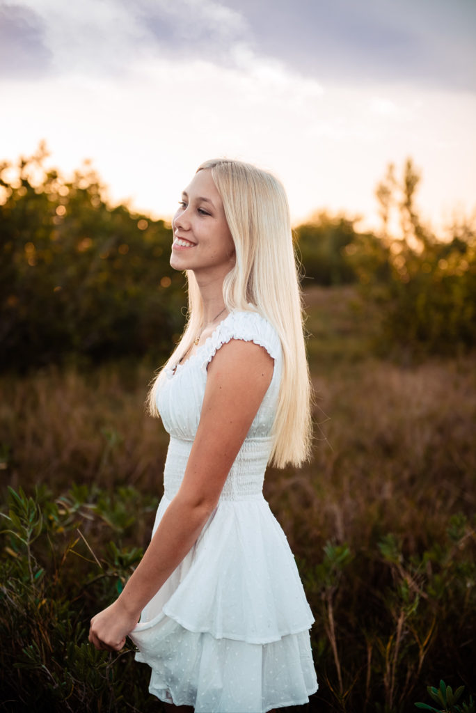 blonde girl in white dress posing in a field of grass 